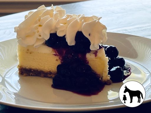 Slice of cheesecake topped with whipped cream and berry compote on a white plate.